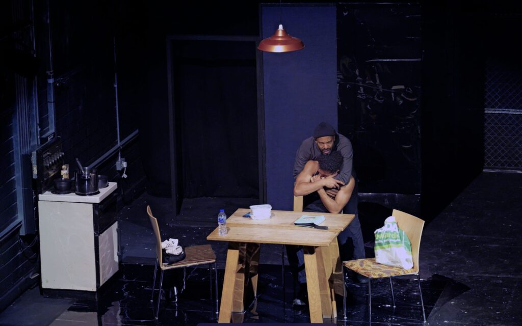 Two WITNESS performers embracing in a stage scene